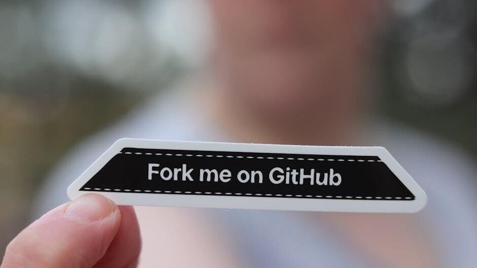 Close-up of a hand holding a 'Fork me on GitHub' sticker, blurred background.