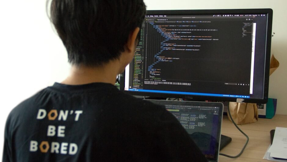 man in black shirt using laptop computer and flat screen monitor