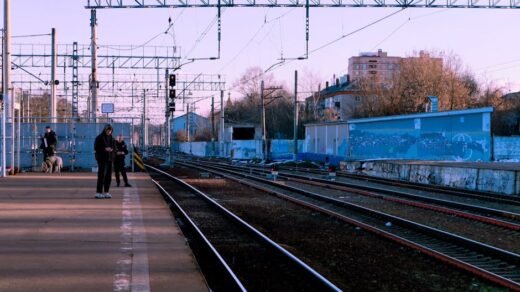 A calm train station scene with people waiting on the platform during the day.