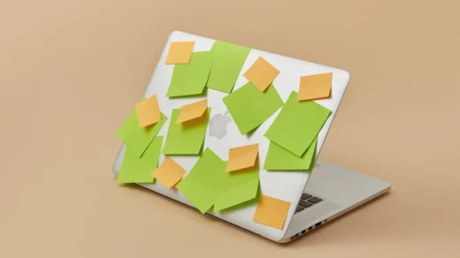 A laptop with its top panel covered in vibrant green and yellow sticky notes, isolated on a beige background.