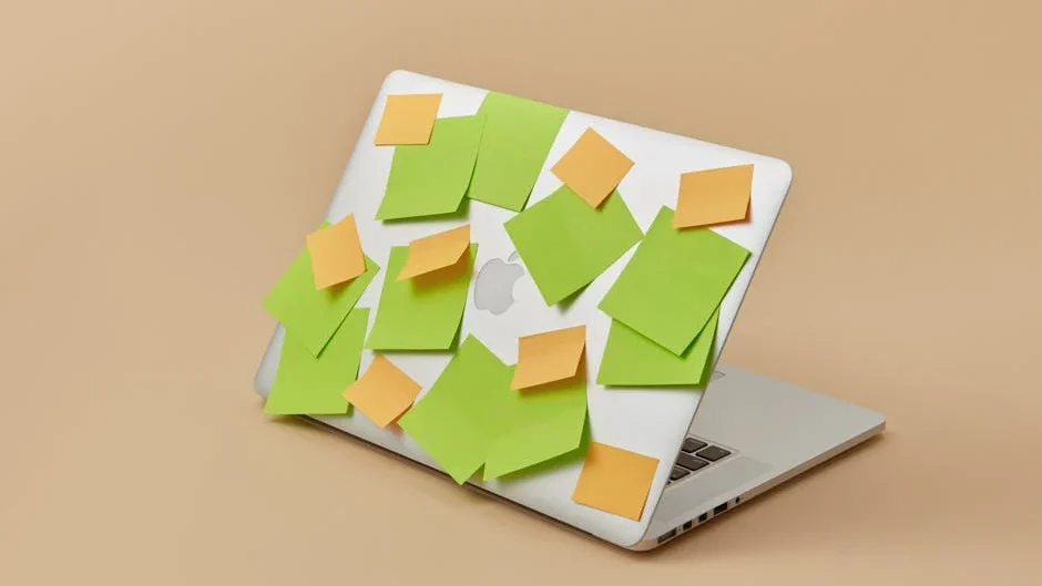 A laptop with its top panel covered in vibrant green and yellow sticky notes, isolated on a beige background.