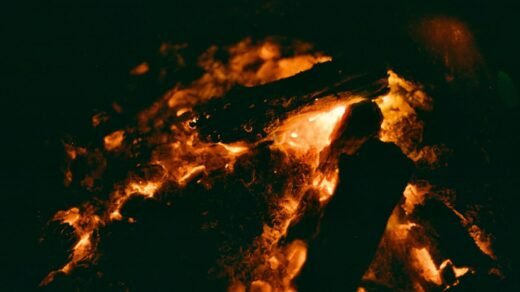 A person silhouetted near a glowing bonfire.