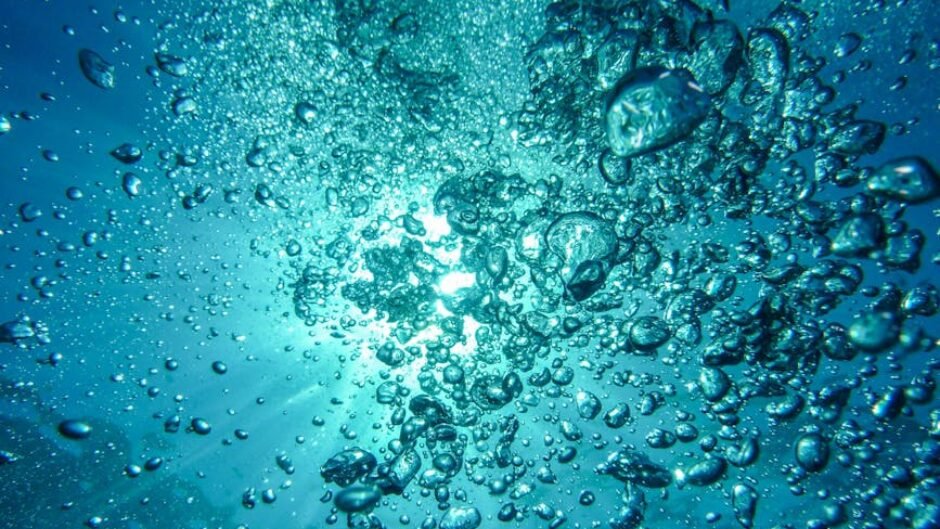 Capture of underwater bubbles rising towards the surface with sunlight streaming through.
