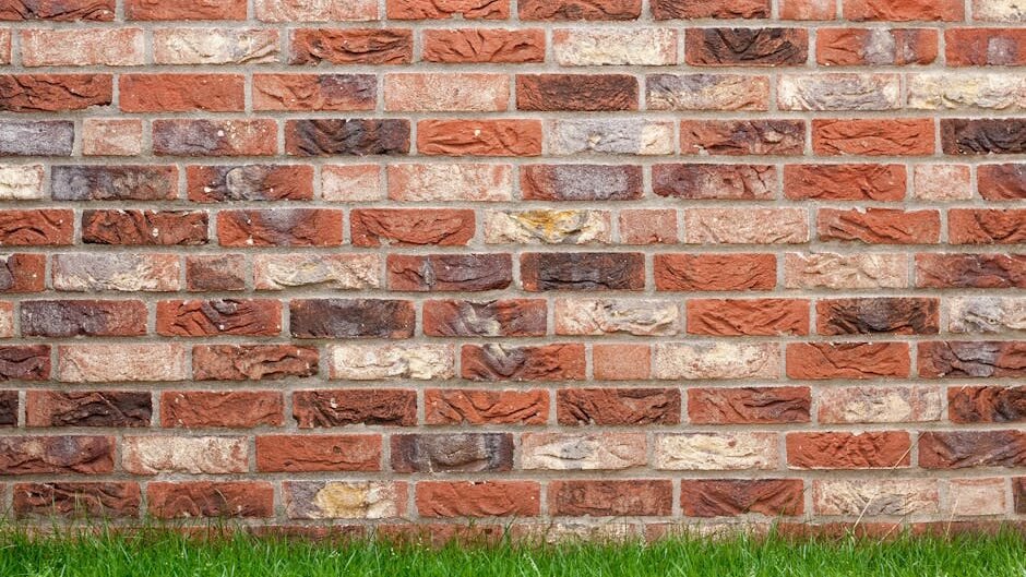 A textured red brick wall with fresh green grass at the base, ideal for backgrounds.