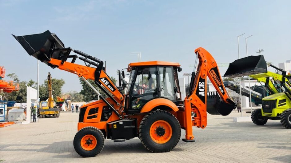 Bright orange ACE AX 124 backhoe loader on display at an outdoor exhibition in India.