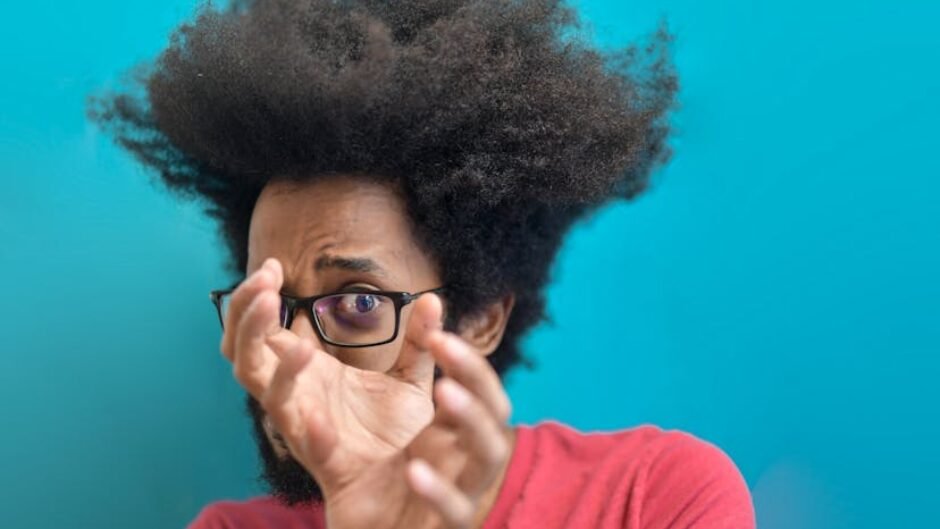 Astonished man with afro hairstyle and glasses in front of a blue background.