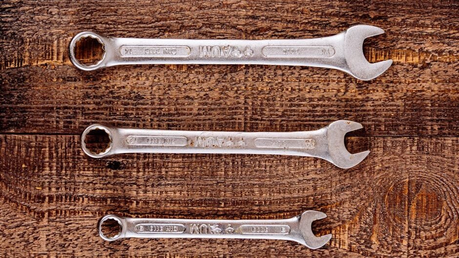 Three metallic wrenches arranged on a rustic wooden table, top view.