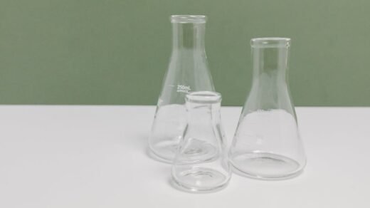 A set of three clear glass laboratory flasks on a clean white and green background, ideal for science themes.