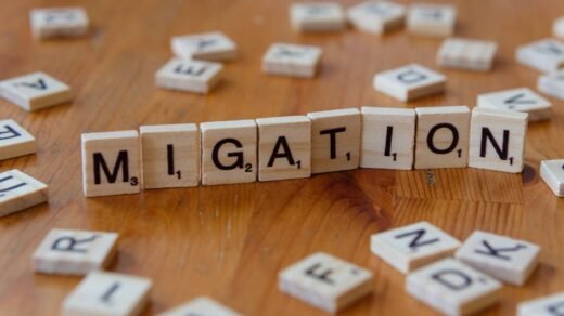 Wooden Scrabble tiles spelling 'Migration' with scattered letters on a wooden table.