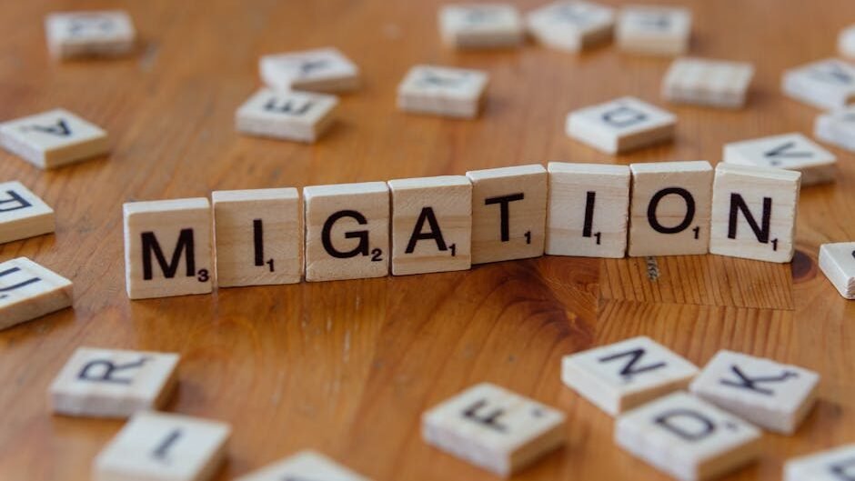 Wooden Scrabble tiles spelling 'Migration' with scattered letters on a wooden table.