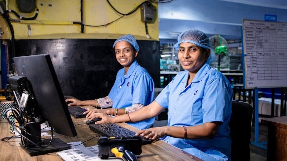 Two female workers at a textile factory operating computers in an industrial setting.