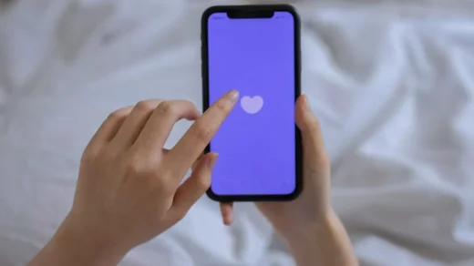 Close-up of hands using a smartphone with a heart icon on screen, representing technology and connection.