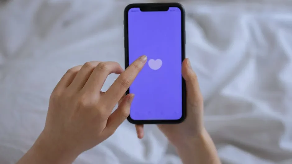 Close-up of hands using a smartphone with a heart icon on screen, representing technology and connection.
