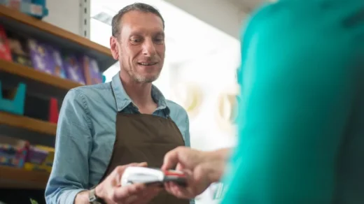 A male store clerk assisting a customer with a payment transaction in a retail shop setting.