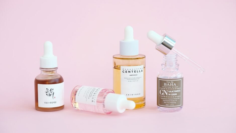 Skincare serums and dropper bottles sit on pink.