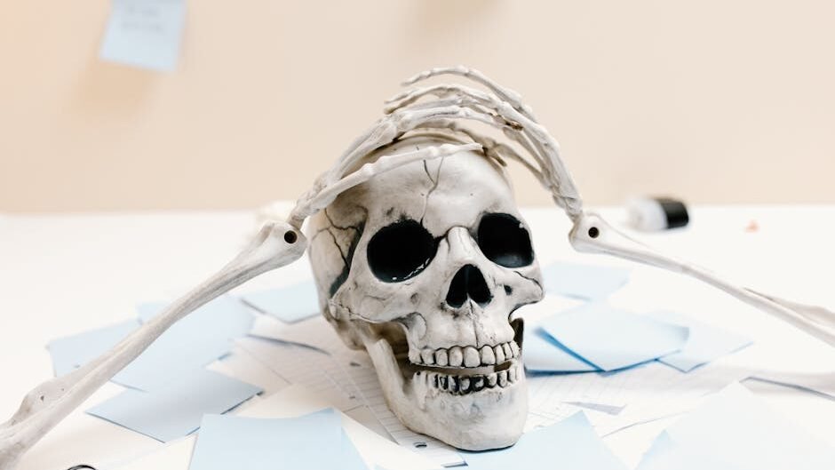 A skeleton rests on a desk with papers, symbolizing exhaustion and overwork.