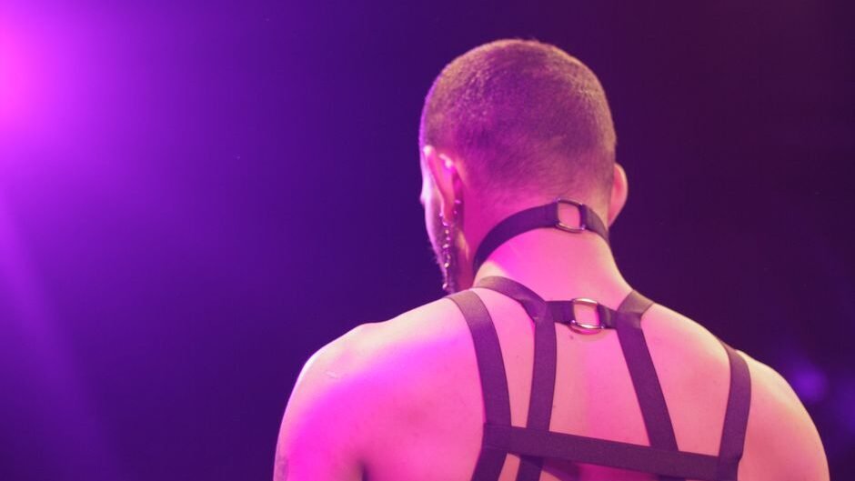 A man's back with fashionable harness captured under vibrant pink lighting.