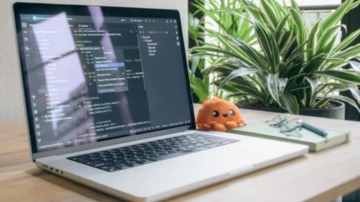 A modern home office setup featuring a laptop with coding software, a plant, and a plush toy.