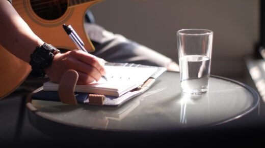 person holding pen writing on white paper beside clear drinking glass